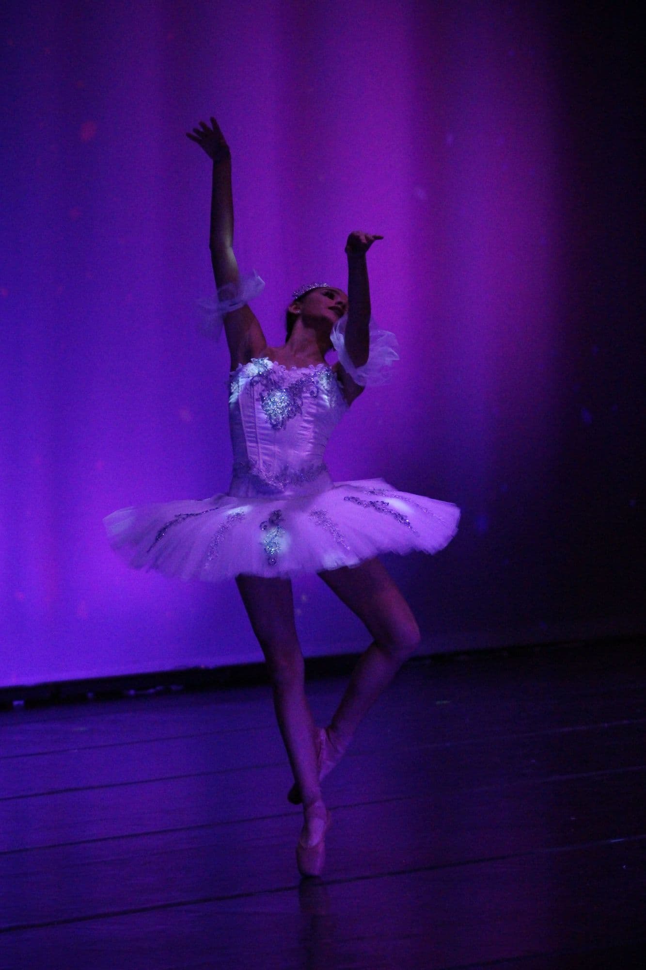 Ballerina in a white tutu dancing en pointe under purple stage light