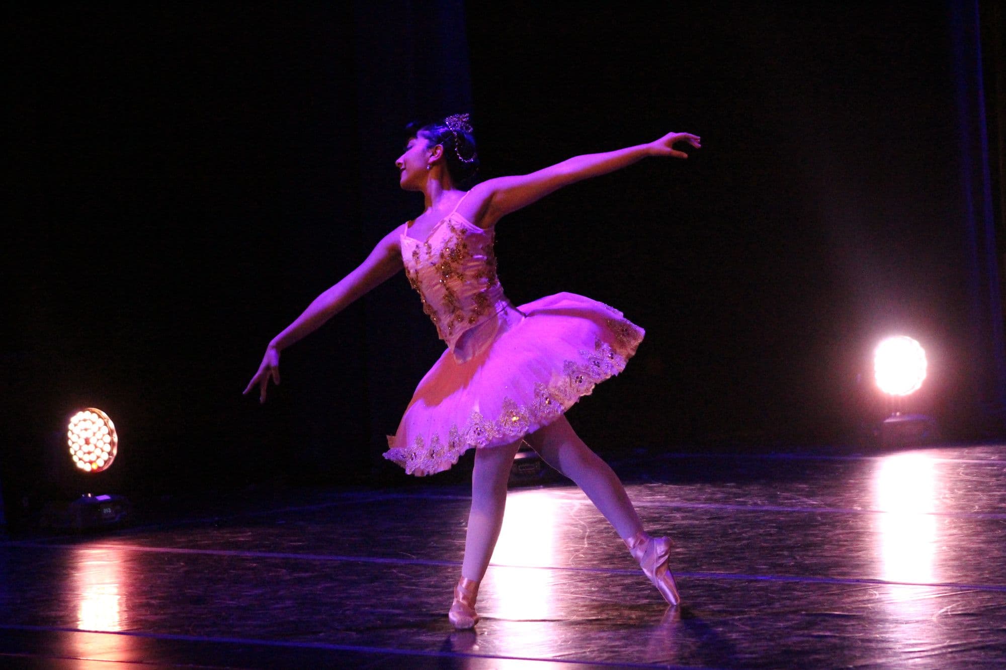 DIDC ballet soloist in a pink and gold tutu extending into an arabesque on stage